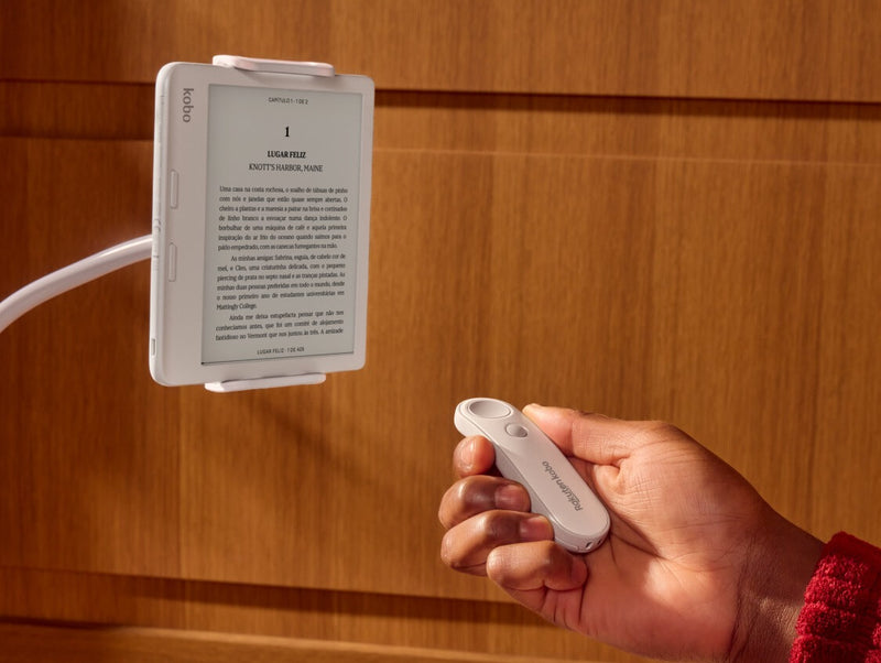 Um Kobo Remote branco é mostrado na mão direita de alguém, apontando para um eReader Kobo Libra Colour branco num suporte flexível.